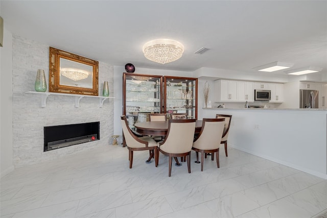 dining room with marble finish floor, visible vents, a stone fireplace, and baseboards