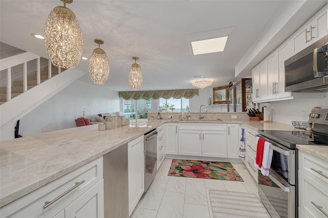 kitchen with light stone counters, stainless steel appliances, hanging light fixtures, white cabinetry, and a sink