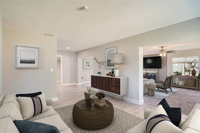 living room with ceiling fan, a fireplace, a textured ceiling, and light hardwood / wood-style flooring