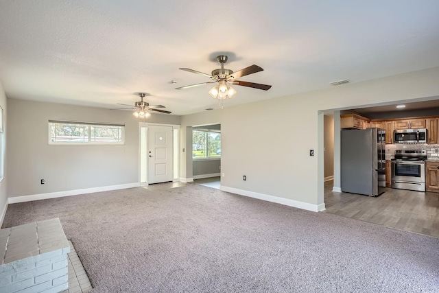 unfurnished living room featuring ceiling fan, a healthy amount of sunlight, and light carpet