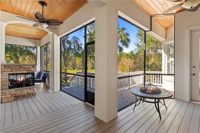 unfurnished sunroom featuring a wealth of natural light, ceiling fan, wooden ceiling, and an outdoor stone fireplace