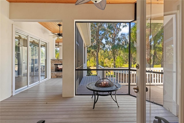 sunroom with ceiling fan and an outdoor stone fireplace