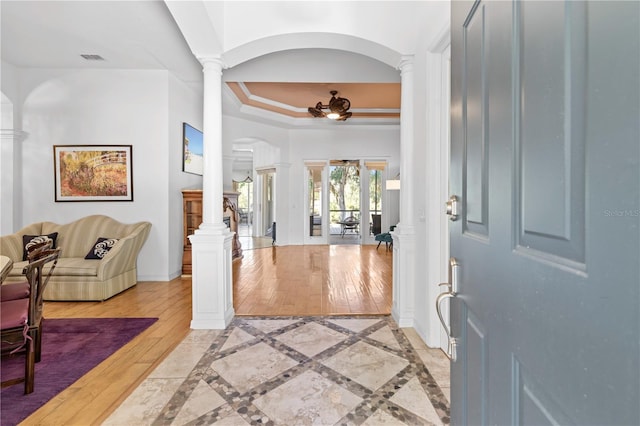 foyer entrance featuring light hardwood / wood-style floors, a raised ceiling, crown molding, and decorative columns