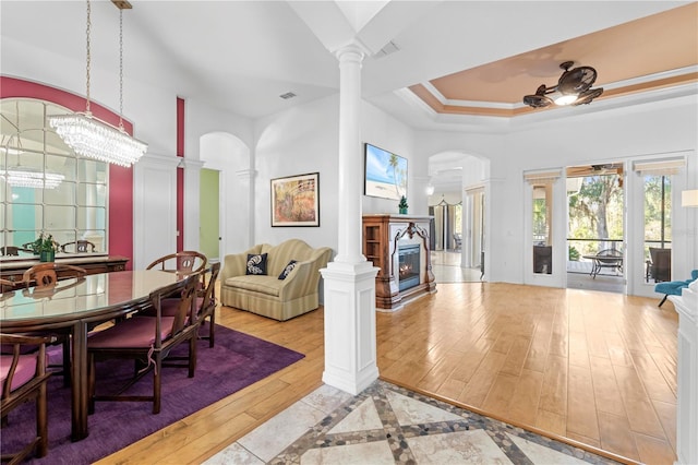 interior space featuring a chandelier, a raised ceiling, light hardwood / wood-style flooring, and ornate columns