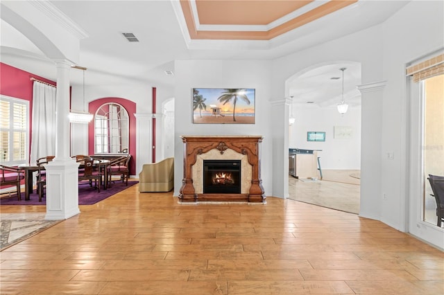 living room with a high end fireplace, light hardwood / wood-style floors, a raised ceiling, and ornamental molding