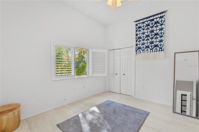 bedroom featuring a towering ceiling, light hardwood / wood-style flooring, a closet, and ceiling fan