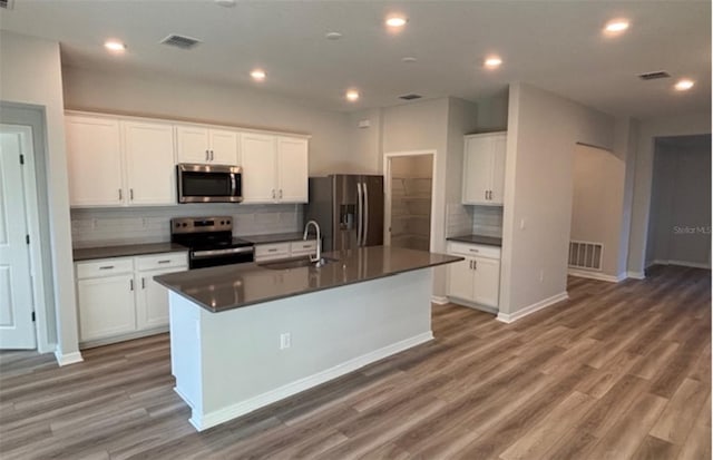 kitchen with stainless steel appliances, a center island with sink, decorative backsplash, dark hardwood / wood-style flooring, and white cabinetry