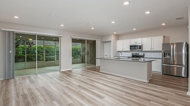 kitchen featuring an island with sink, appliances with stainless steel finishes, white cabinets, and decorative backsplash