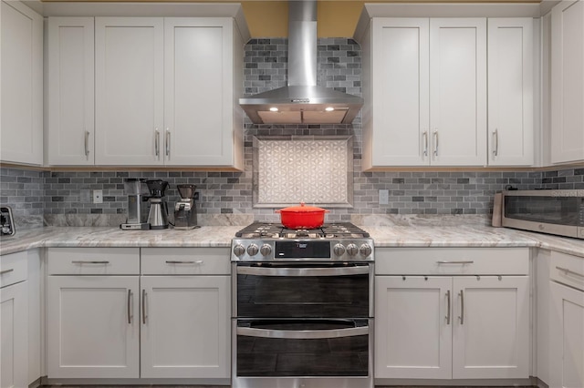 kitchen featuring gas range, wall chimney exhaust hood, light stone counters, decorative backsplash, and white cabinets