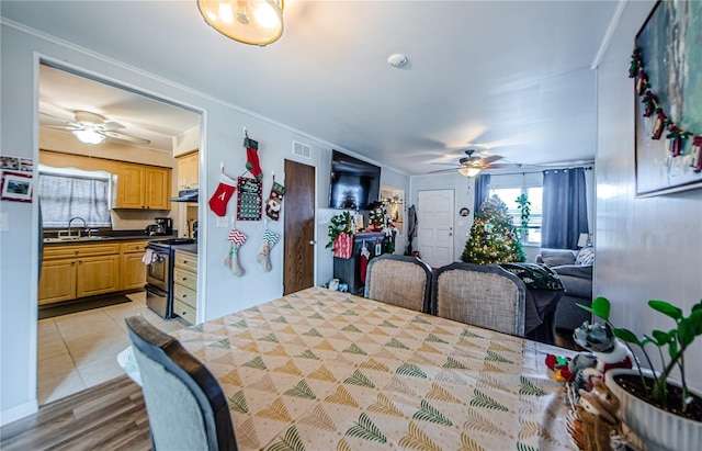 dining space featuring light tile patterned flooring, ceiling fan, crown molding, and sink