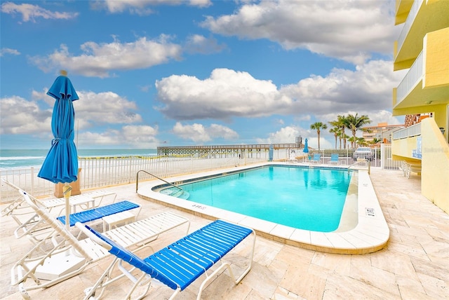 view of swimming pool featuring a patio, a water view, and a beach view