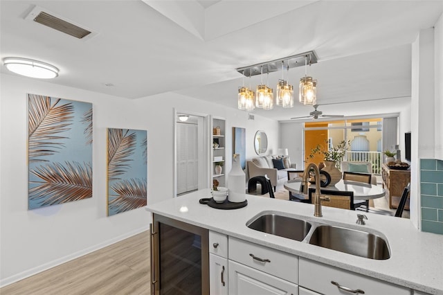 kitchen featuring sink, white cabinets, beverage cooler, hanging light fixtures, and light stone countertops