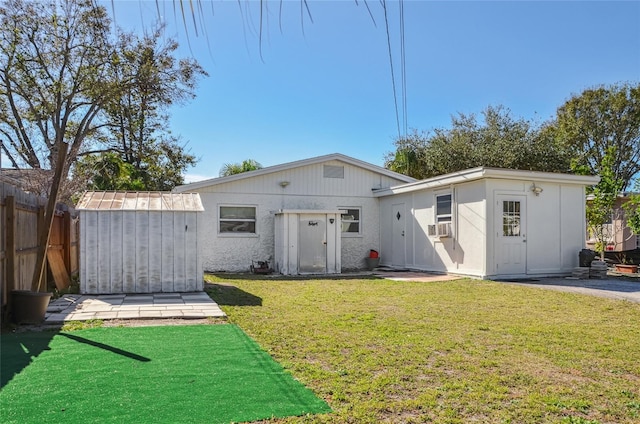 rear view of property featuring cooling unit, a storage unit, and a lawn