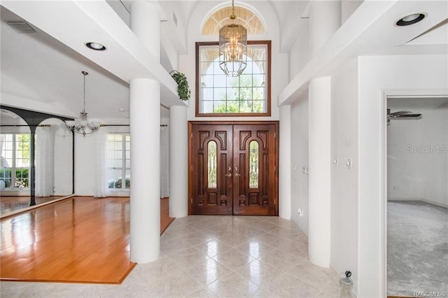 entryway featuring light hardwood / wood-style floors, ornate columns, a high ceiling, and an inviting chandelier