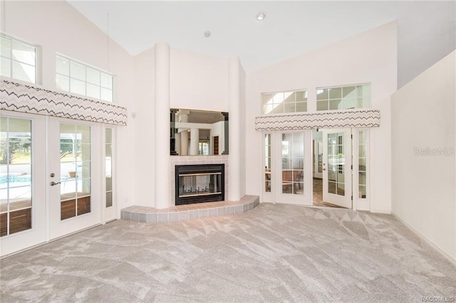 unfurnished living room with carpet floors, a tile fireplace, french doors, and high vaulted ceiling