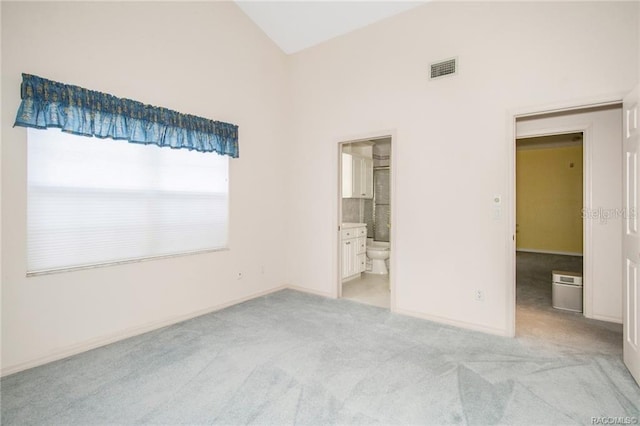 unfurnished bedroom with ensuite bathroom, high vaulted ceiling, and light colored carpet