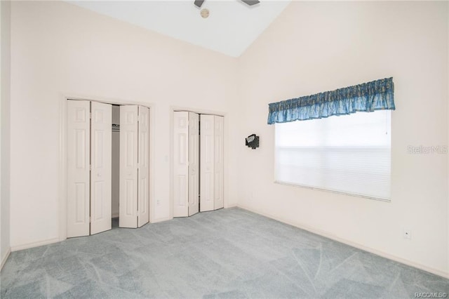 unfurnished bedroom with multiple closets, light carpet, and high vaulted ceiling