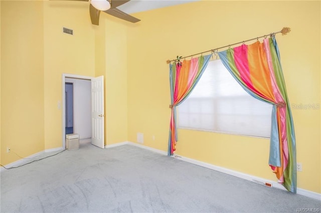 carpeted spare room featuring a high ceiling and ceiling fan