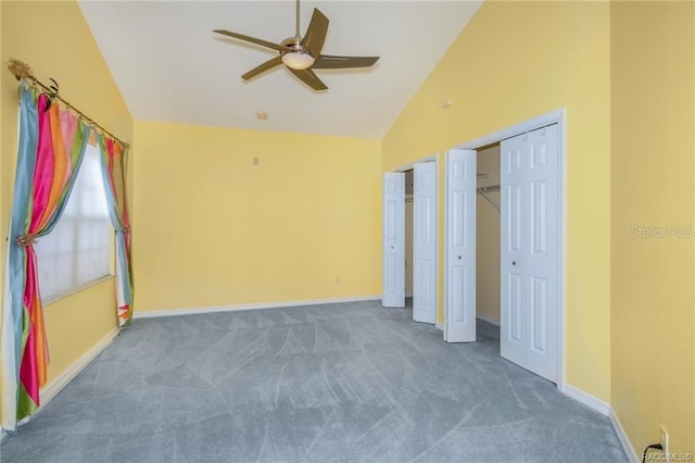 unfurnished bedroom featuring ceiling fan, dark carpet, high vaulted ceiling, and two closets