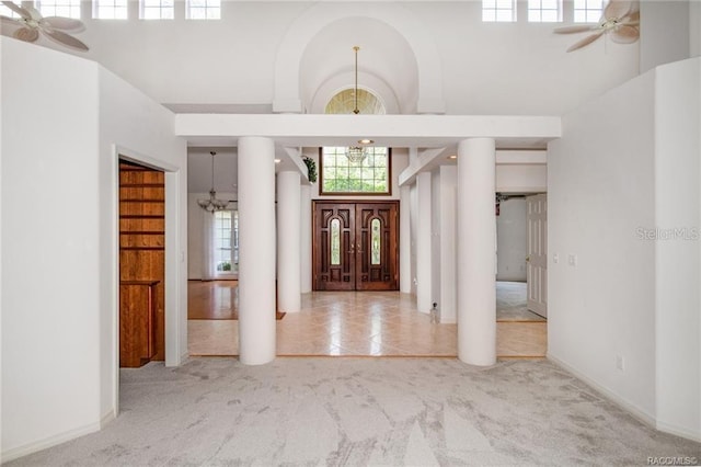 foyer featuring ceiling fan with notable chandelier, light colored carpet, and a high ceiling