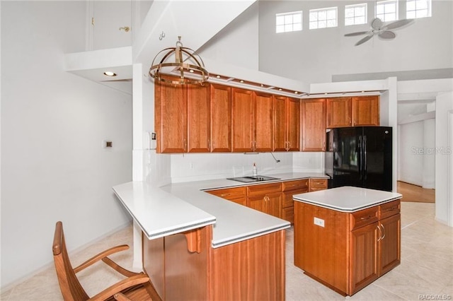 kitchen featuring a center island, black fridge, ceiling fan, a towering ceiling, and kitchen peninsula