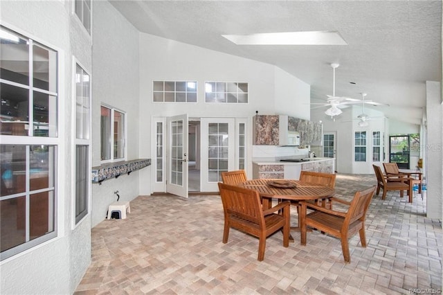 dining room featuring a skylight, ceiling fan, french doors, high vaulted ceiling, and a textured ceiling