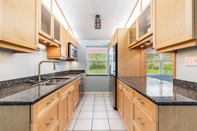 kitchen featuring sink, dark stone countertops, a textured ceiling, appliances with stainless steel finishes, and light tile patterned flooring