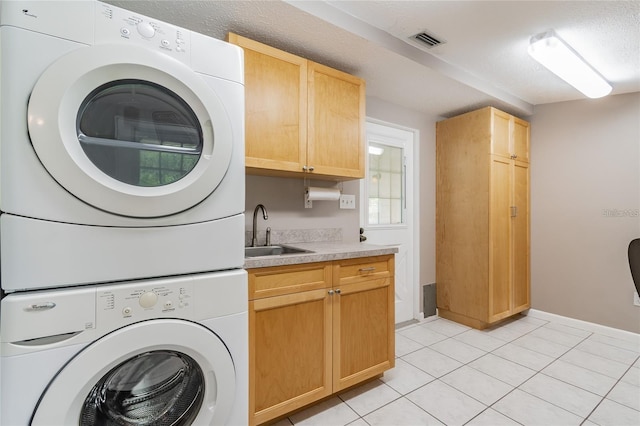 washroom with sink, cabinets, stacked washer and dryer, a textured ceiling, and light tile patterned floors