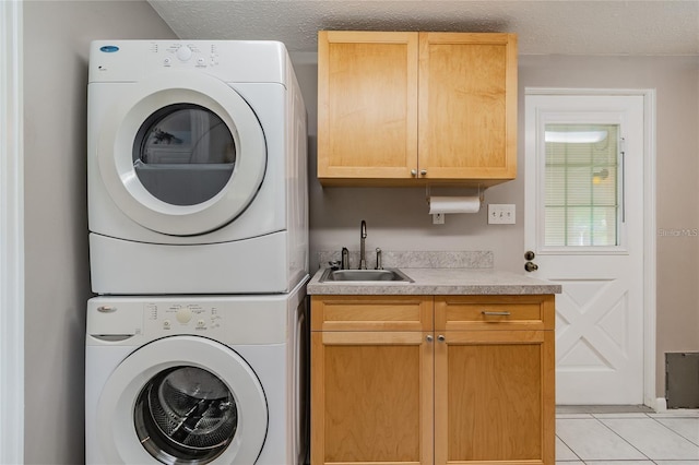 laundry room with sink, cabinets, a textured ceiling, light tile patterned floors, and stacked washer and clothes dryer