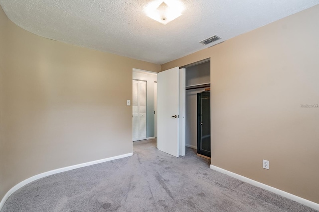 unfurnished bedroom featuring a textured ceiling, light carpet, and a closet