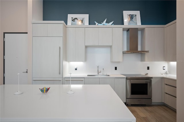 kitchen featuring sink, white cabinetry, stainless steel electric range oven, light hardwood / wood-style floors, and wall chimney range hood