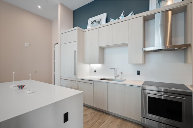 kitchen with sink, paneled built in fridge, light hardwood / wood-style floors, wall chimney range hood, and stainless steel electric range