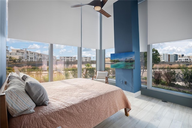 bedroom with light hardwood / wood-style floors, ceiling fan, and a water view