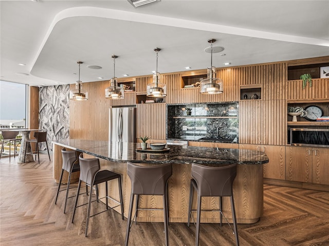 kitchen featuring parquet floors, hanging light fixtures, stainless steel refrigerator, and a breakfast bar area