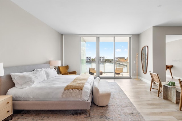 bedroom with a water view, floor to ceiling windows, light wood-type flooring, and access to outside