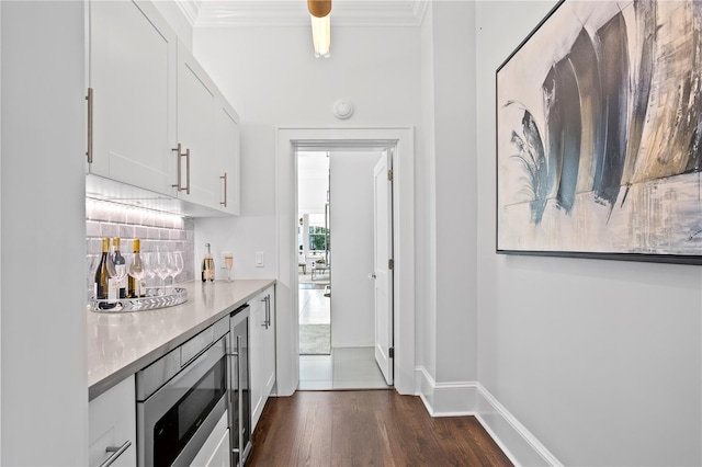 bar featuring stainless steel microwave, tasteful backsplash, dark hardwood / wood-style flooring, crown molding, and white cabinets