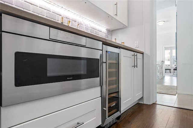 kitchen featuring stainless steel microwave, white cabinetry, dark wood-type flooring, and beverage cooler