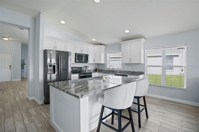 kitchen featuring appliances with stainless steel finishes, dark stone counters, white cabinets, a center island, and lofted ceiling