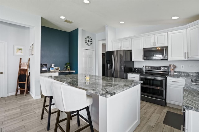 kitchen featuring appliances with stainless steel finishes, vaulted ceiling, white cabinetry, and dark stone countertops