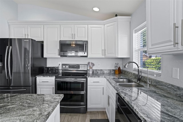 kitchen with appliances with stainless steel finishes, vaulted ceiling, sink, light hardwood / wood-style flooring, and white cabinets