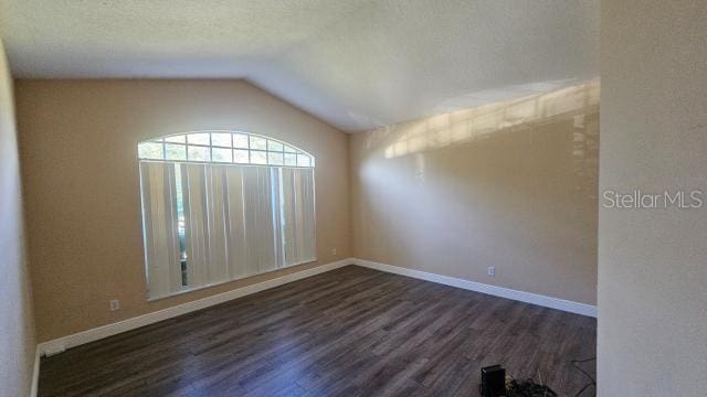 spare room with a textured ceiling, dark wood-type flooring, and vaulted ceiling