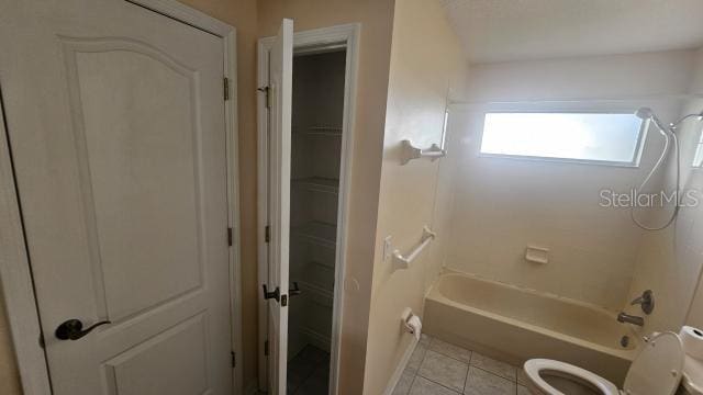 bathroom with tile patterned flooring, toilet, and washtub / shower combination