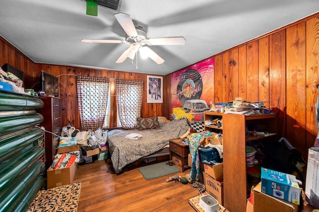 bedroom with hardwood / wood-style flooring, ceiling fan, and wooden walls