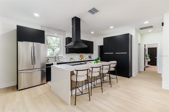 kitchen with a kitchen island, light wood-type flooring, range hood, and stainless steel refrigerator