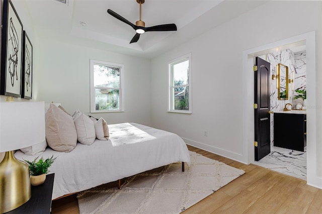 bedroom with hardwood / wood-style flooring, ceiling fan, and a tray ceiling