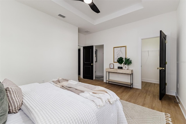 bedroom with a raised ceiling, a walk in closet, ceiling fan, wood-type flooring, and a closet