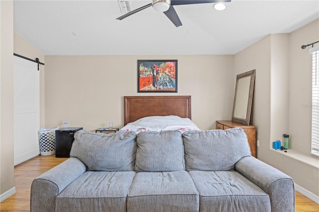 bedroom featuring light wood-type flooring, a barn door, and ceiling fan