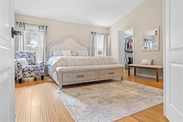 bedroom with a spacious closet, a closet, wood-type flooring, and vaulted ceiling