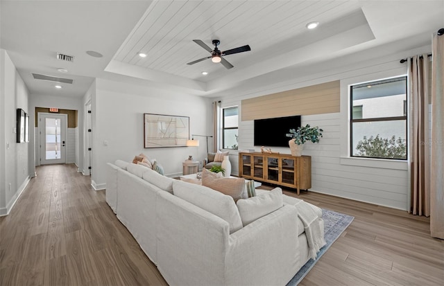 living room with light hardwood / wood-style flooring, a raised ceiling, and a healthy amount of sunlight