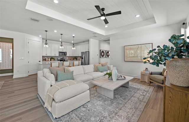 living room featuring a raised ceiling, ceiling fan, wood ceiling, and light hardwood / wood-style floors